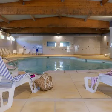 Piscine intérieure du Camping Le Ried avec chaises longues et sacs à main.