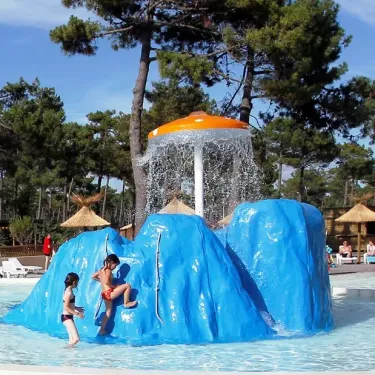 Enfant jouant sur un toboggan aquatique bleu sous une fontaine à effet pluie au Camping Atlantique Club Montalivet.