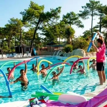 Camping Atlantique Club Montalivet : groupe faisant de l'eau avec des bouées colorées dans une piscine entourée d'arbres.