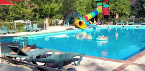 Piscine avec toboggan coloré et chaises longues au Camping Fontaine du Roc