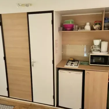 Tithome 2 Chambres 4 Personnes Sans Sanitaires - Camping des Bastides : cuisine compacte avec réfrigérateur, four à gaz et micro-ondes.
