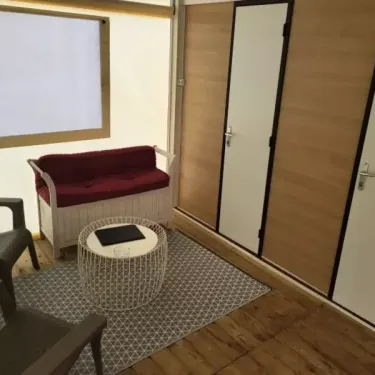 Tithome 2 Chambres 4 Personnes Sans Sanitaires - Camping des Bastides : salon avec canapé, table ronde et tapis en tissu.