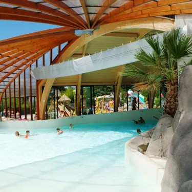 Piscine couverte avec structure en bois et palmiers artificiels, Camping La Rive