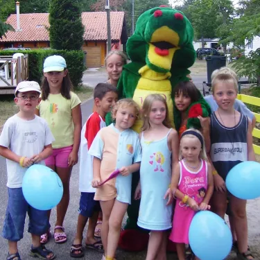 Enfants souriants avec mascotte serpent au Camping Lou Puntaou, tenant des ballons.