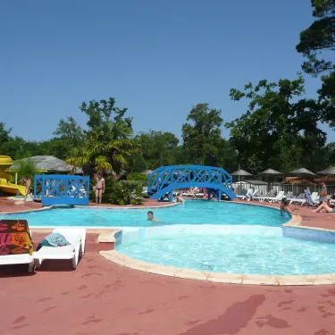 Piscine avec pont bleu et chaises longues autour, au Camping Lou Puntaou.
