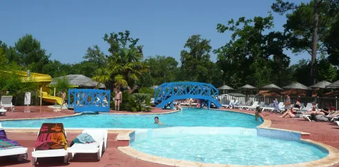 Piscine avec pont bleu et chaises longues autour, au Camping Lou Puntaou.