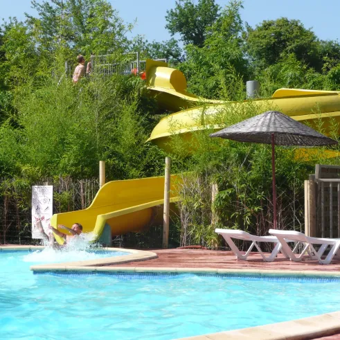 Un enfant descend une grande slide jaune dans la piscine du Camping Lou Puntaou.