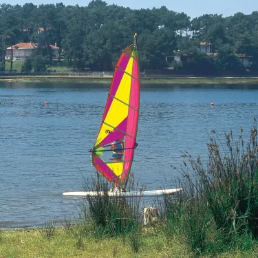 Camping Lou Puntaou - Personne pratiquant le windsurf sur un lac entouré d'arbres.