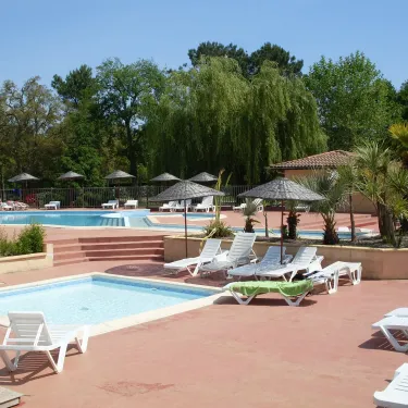 Camping Lou Puntaou : piscine entourée de chaises longues sous parasols.
