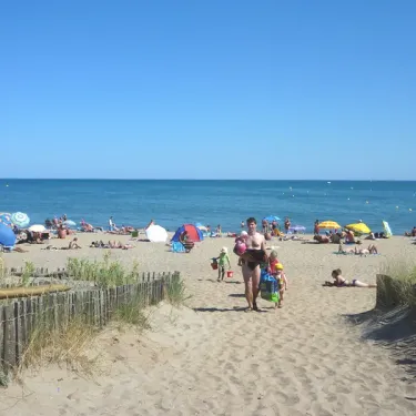 Camping La Plage et le Bord de Mer : plage ensoleillée avec parasols et baigneurs.