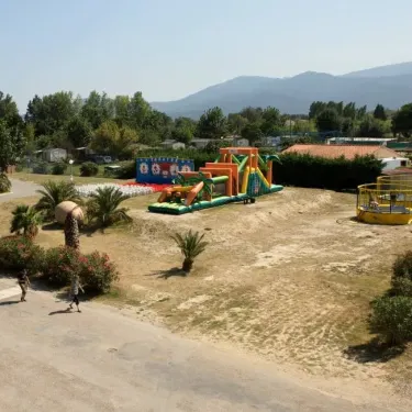 Camping Le Littoral : parc d'attractions gonflables avec montagnes russes et palmiers.