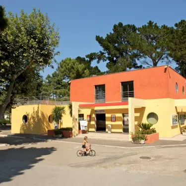 Camping Le Littoral - bâtiment jaune et orange avec enfant en vélo