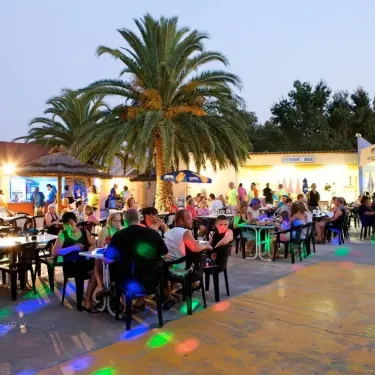 Terrasse de restaurant animée avec palmiers et lumières colorées au Camping Le Littoral