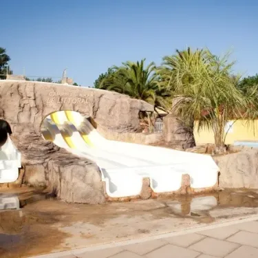Camping Le Littoral : toboggan aquatique blanc intégré dans un décor rocheux avec palmiers.