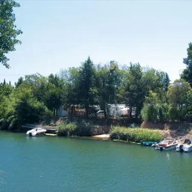 Camping La Barque avec embarcations sur un lac entouré de verdure.
