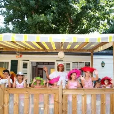 Enfants au Camping La Barque : groupe souriant sous une pergola à l'extérieur d'une cabane mobile.