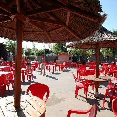 Terrasse avec parasols en paille et chaises rouges au Camping L’Europe