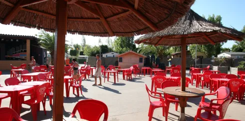 Terrasse avec parasols en paille et chaises rouges au Camping L’Europe