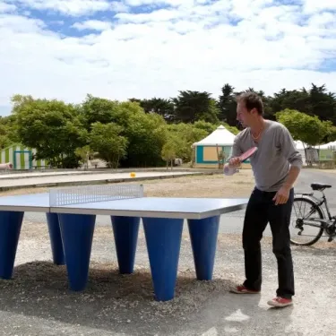 Camping La Côte Sauvage : deux personnes jouant au ping-pong en plein air avec des tentes en arrière-plan.