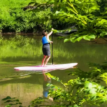 Personne en stand-up paddle sur une rivière ombragée, Camping La Boissière