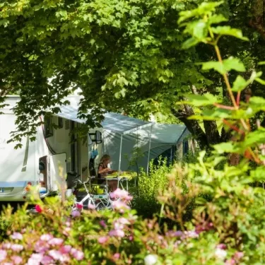 Camper avec une caravane et une tente sous les arbres au Camping La Boissière.