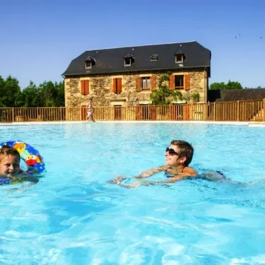 Enfants dans la piscine au Camping La Boissière, avec une maison en pierre en arrière-plan.