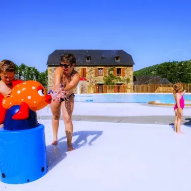 Enfants jouent aux jeux d'eau sur le bord de la piscine à Camping La Boissière, avec des structures colorées.