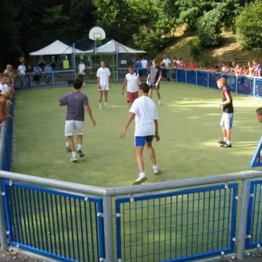Terrain de basket-ball en herbe artificielle au Camping Bela Basque, encerclé de spectateurs.