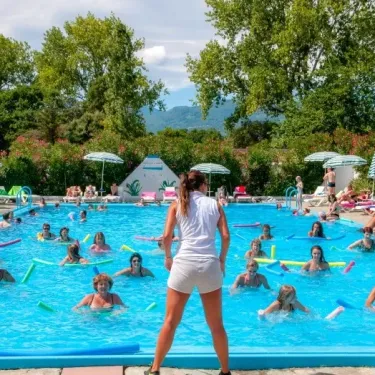 Camping Domaine d'Anghione : groupe faisant de l'exercice aquatique dans la piscine entourée d'arbres et de parasols.