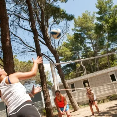 Jeux de volley-ball en plein air dans le camping Le Castellas, entouré de pins.