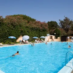 Camping Domaine d'Anghione : piscine extérieure avec des visiteurs nageant, parasols bleus et arbres fleuris en arrière-plan.