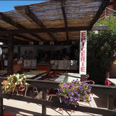 Épicerie extérieure avec tables et chaises sous une pergola en paille au Camping Le Soleil Bleu.