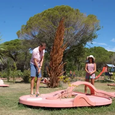Camping Oasis Village : couple jouant au mini-golf dans un parc verdoyant.
