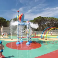 Zone de jeux aquatique colorée avec fontaines et arches au Camping Oasis Village, enfants s'amusent.