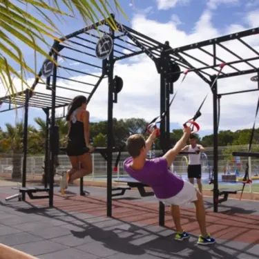 Camping Oasis Village : personnes faisant de l'exercice sur un équipement extérieur sous palmiers.