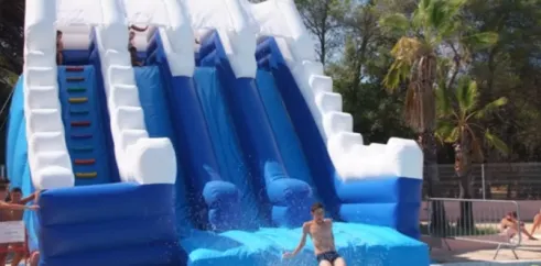 Glisseur gonflable bleu et blanc au Camping Oasis Village, enfants qui descendent dans la piscine.