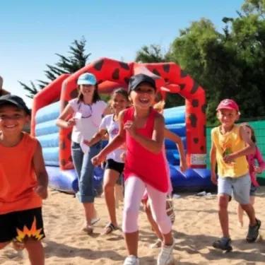 Enfants qui courrent sur le sable près d'un parcours gonflable au Camping Les Paludiers
