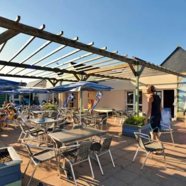 Camping Les Paludiers - Terrasse avec parasols et tables sous une pergola