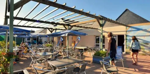 Camping Les Paludiers - Terrasse avec parasols et tables sous une pergola