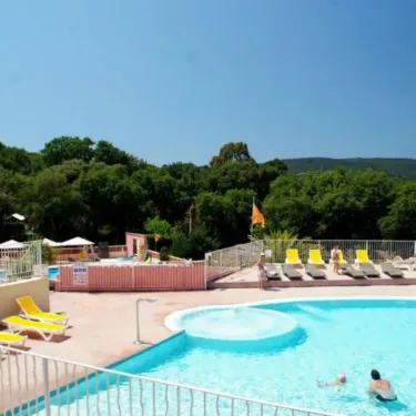 Piscine avec chaises longues jaunes et vue sur les arbres au Camping Parc Montana