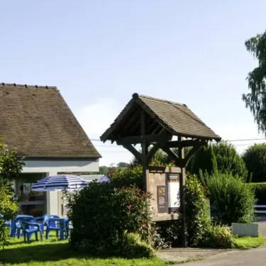 Entrée du camping avec tables bleues, parasol rayé et kiosque en bois, Camping Le Bois d'Emeraude