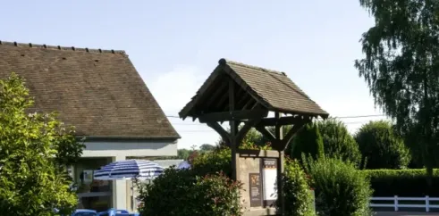 Entrée du camping avec tables bleues, parasol rayé et kiosque en bois, Camping Le Bois d'Emeraude