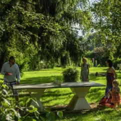 Famille jouant au ping-pong dans un espace vert ombragé, Camping Le Bois d'Emeraude