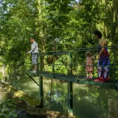 Une famille sur un pont en bois au-dessus d'un cours d'eau, Camping Le Bois d'Emeraude