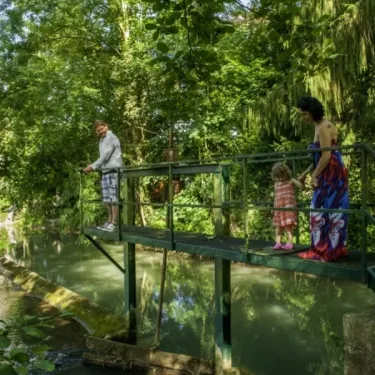 Une famille sur un pont en bois au-dessus d'un cours d'eau, Camping Le Bois d'Emeraude