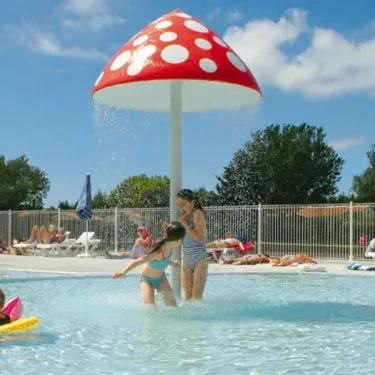 Enfants jouent sous la fontaine champignon dans la piscine du Camping Les Ilates