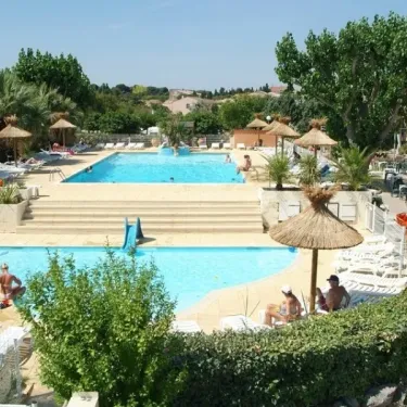 Piscine avec toboggan et personnes nageant, parasols en paille autour au Camping Beau Rivage.