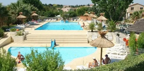 Piscine avec toboggan et personnes nageant, parasols en paille autour au Camping Beau Rivage.