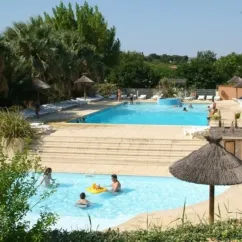 Piscine avec enfants et adultes à Camping Beau Rivage, entourée de palmiers et d'ombrelles en paille.