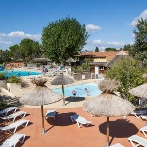 Piscine avec parasols en paille et chaises longues au Camping Beau Rivage sous un ciel bleu.